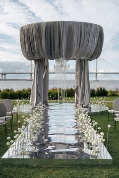 an outdoor ceremony setup with white flowers and draping on the top, water running down the aisle