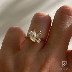 a person's hand holding a ring with two pear shaped diamonds on top of it