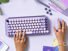 a woman using a purple keyboard and mouse on a white desk with other office supplies