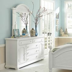 a white dresser sitting next to a bed in a room with blue walls and windows