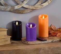 three candles sitting on top of a wooden table next to books and a cell phone