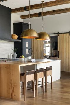 a kitchen with two pendant lights hanging from the ceiling and wooden stools in front of an island