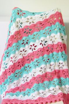 a crocheted blanket sitting on top of a wooden table next to a white wall