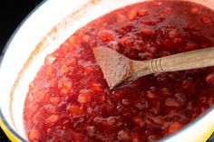 a wooden spoon in a pot filled with red sauce