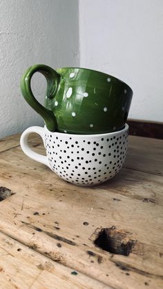 two green and white polka dot mugs sitting on top of a wooden table next to each other