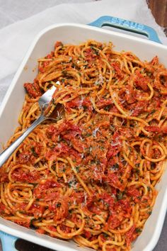 a blue and white casserole dish filled with spaghetti, tomato sauce and spinach