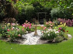 a garden filled with lots of flowers next to a stone path through a lush green field