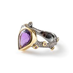 This ring from the Bacchus Bunch Collection by designer German Kabirski is made of 925 Silver, plated with 18K Gold and Black Rhodium, and features a large pear-cut natural Amethyst. Inspired by Bacchus, the Roman god of wine, festivity, and artistic performance, this ring embodies the spirit of joy and celebration. Amethyst is believed to bring balance, calm, and clarity to its wearer. Ideal for those who love life and happiness. Metal: 925 Silver Stones: Amethyst Plating: Black Rhodium, 18K Gold  PLEASE NOTE: The raw gemstones have natural imperfections such as cracks and color spots, which are signs of authenticity. They may also appear differently under various lighting conditions. July Birthstone Jewelry, August Birthstone Jewelry, Fine Art Jewelry, Gold Gifts, Pearl Jewellery Earrings, Jewelry Ring Box, Black Rhodium, Men's Jewelry Rings, Evil Eye Jewelry