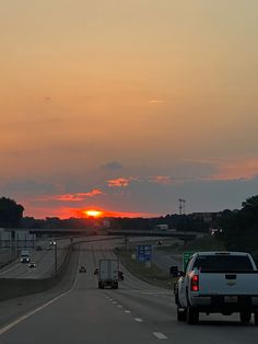 the sun is setting over an interstate with cars driving down it's lane and trees in the background