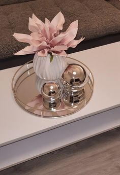 a white vase with pink flowers sitting on top of a mirrored tray in front of a couch