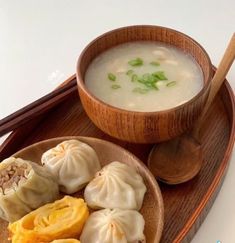 a wooden plate topped with dumplings next to a bowl of soup and chopsticks