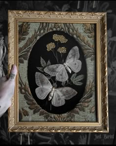 a person holding up a framed painting with moths on it's wings and leaves