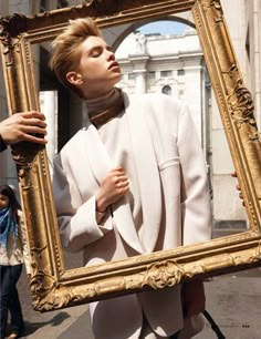 a woman holding up a gold frame with a man's face in the reflection