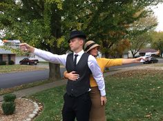 a man and woman dressed up in costume pointing at something on the street with trees behind them