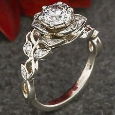 a close up of a ring with a flower on the side and a red rose in the background