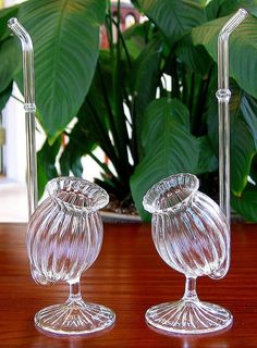 two clear glass vases sitting on top of a wooden table next to a plant