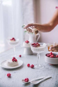 a woman is pouring raspberries into a dessert