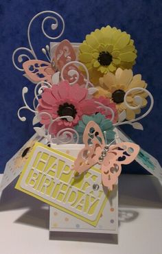 a birthday card with flowers and butterflies in a vase on top of a table next to a blue wall