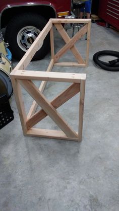 a wooden structure sitting on top of a floor next to a red car in a garage