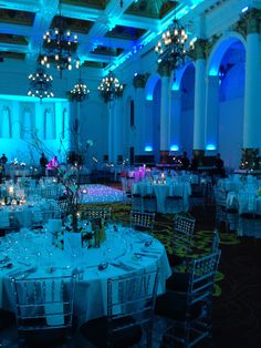 a banquet hall with tables and chairs covered in white linens, lit by blue lights