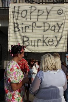 two women standing in front of a sign that says happy birthday bukke on it