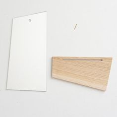 a piece of wood next to a blank tag on a white surface with pins sticking out of it