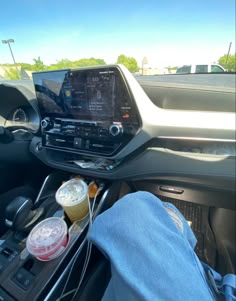 someone is sitting in the car with their feet on the steering wheel, and there are two drinks next to them