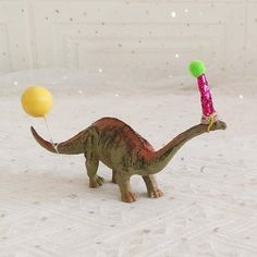 a toy dinosaur with a birthday hat on its head and a balloon in it's mouth