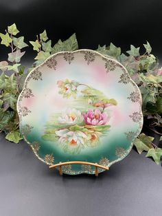 a plate with flowers painted on it sitting next to some leaves and plants in the background