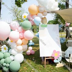 a bunch of balloons that are in the grass near a sign and some flowers on it