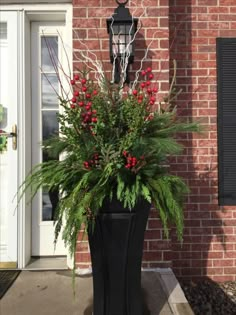 a tall planter with red berries and greenery in front of a brick building