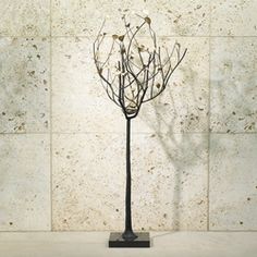 a metal tree with birds on it in front of a white wall and tile floor