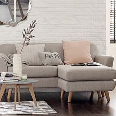 a living room with white brick walls and wood flooring, a gray sectional sofa is surrounded by bookshelves