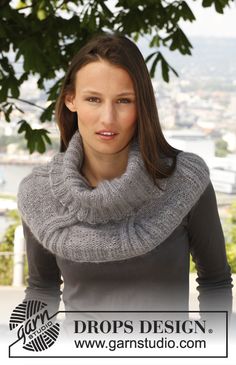 a woman standing under a tree wearing a gray sweater and grey cowl neck scarf