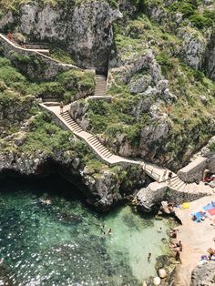 people are swimming in the clear blue water near steps leading to an outdoor area that is surrounded by rocky cliffs