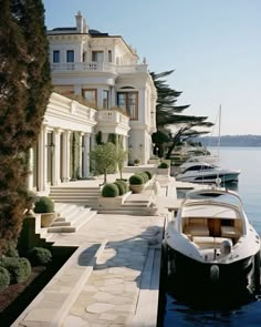 a row of boats parked next to a large white house on the water's edge