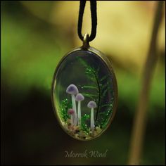 three tiny white mushrooms in a mossy glass dome hanging from a black cord necklace