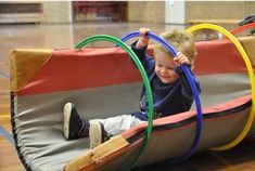 a young boy is playing in an indoor trampoline with colored hooping around his neck