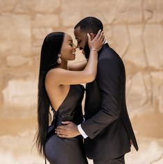 a man and woman embracing each other in front of a stone wall