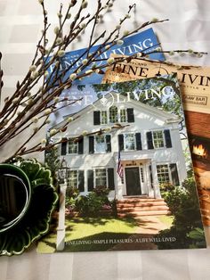 two magazines sitting on top of a bed next to a vase with flowers in it