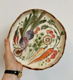 a hand holding a plate with vegetables painted on it