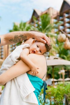 a woman holding a baby in her arms while she is getting her hair brushed by an adult