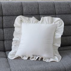 a white pillow with ruffled edges on a gray couch