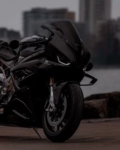 a black motorcycle parked in front of a body of water with buildings in the background