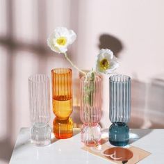 three different colored vases with flowers in them sitting on a white countertop next to a window