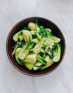 a brown bowl filled with green vegetables on top of a white counter