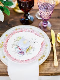 a place setting with plates, napkins and wine glasses on a wooden table top