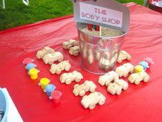 a red table topped with lots of toy cars and buckets filled with sand next to a sign that says the body shop