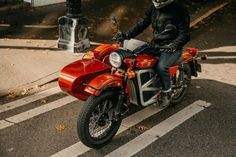 a man riding on the back of a red motorcycle down a street next to a crosswalk