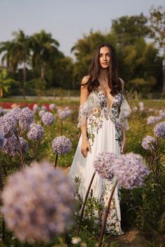 a woman in a white dress standing in a field full of purple and white flowers